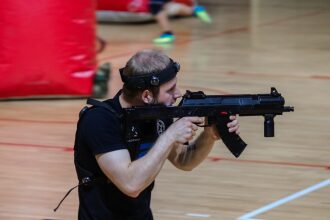 Боец LASERWAR прицеливается из-за красного укрытия.